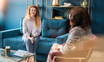 smiling woman sitting on a turquoise couch talking with another woman in a modern interior space designed for conversation and therapy nine different methods for effective communication